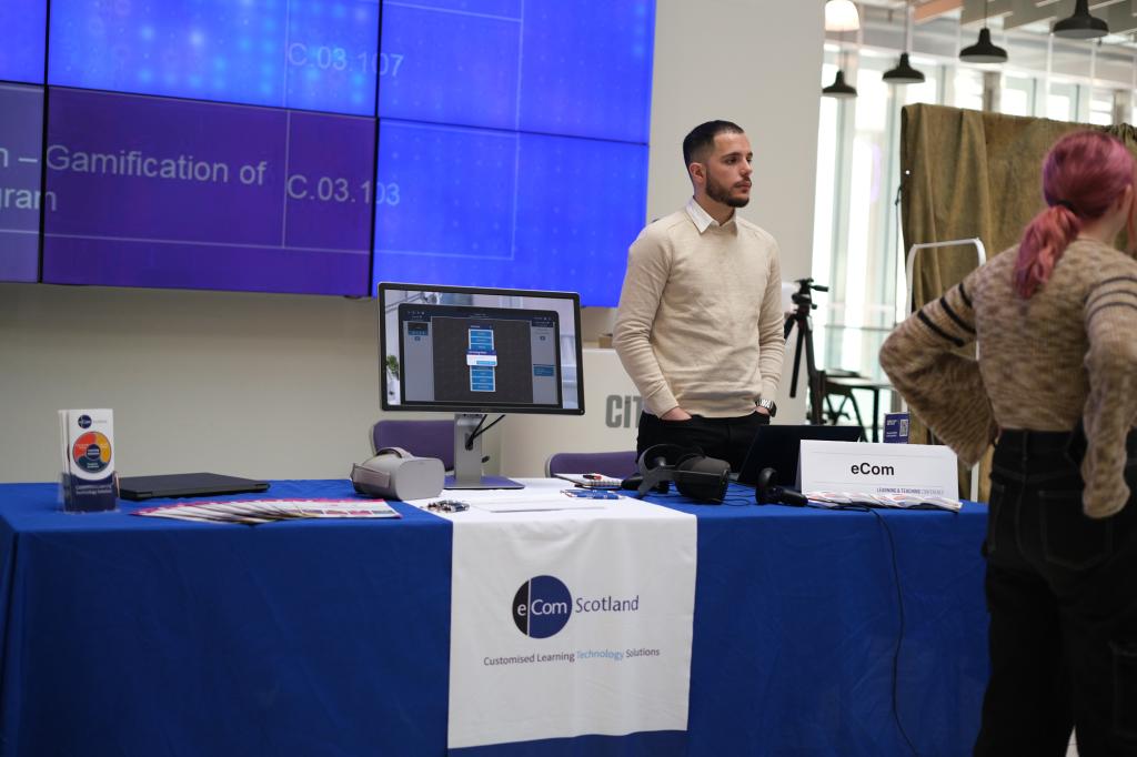 An exhibitor standing in front of a stand with a table covered with a tablecloth