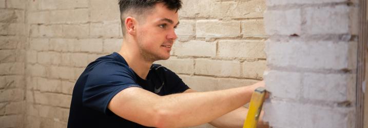 Student using a spirit level against a brick wall.