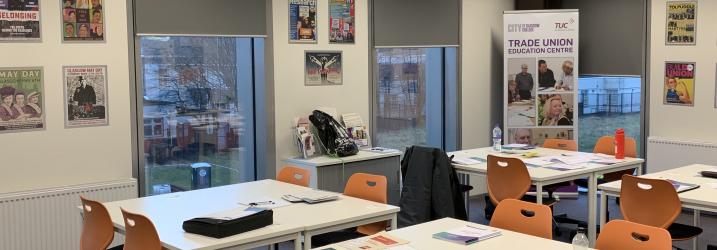 A classroom set up with desks in groups of four and chairs round the desks.