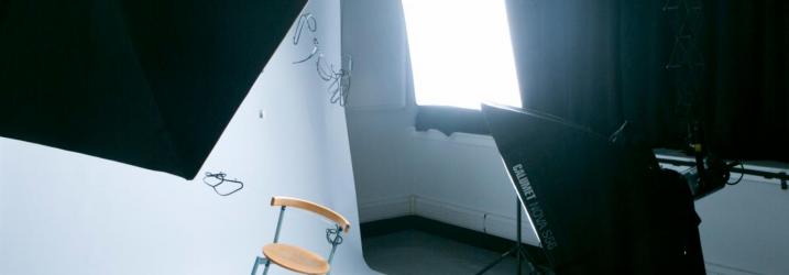 Photography studio set up with lights and a white background with a chair balancing on one leg in the middle.