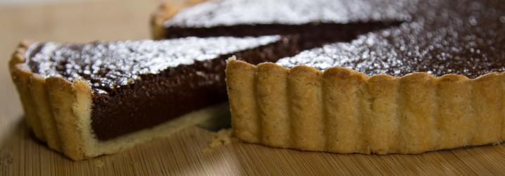 A close up of a chocolate tart with a slice cut out.