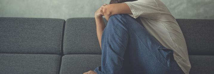 Man crouched on a couch wearing pyjamas