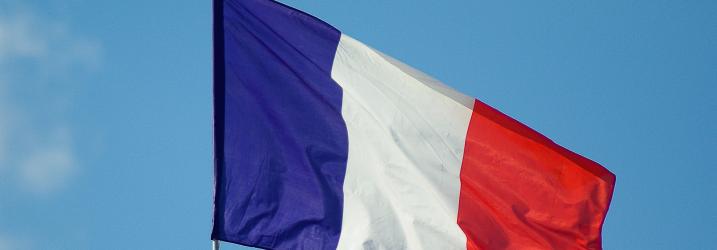 French flag blowing in the wind with clear blue sky in the background.