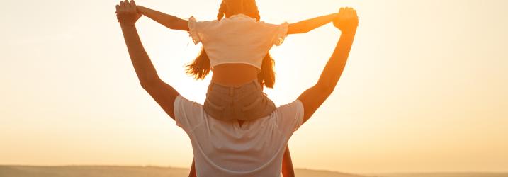 A father with his daughter on his shoulders in the sunset.