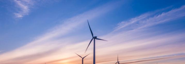 Several wind turbines with blue sky and a bright orange sun in the background.