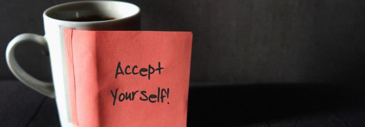 black background with a white cup and red post it with accept yourself written on it