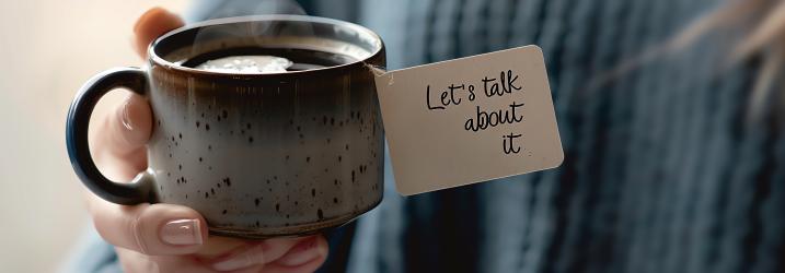 A close-up of a hand holding a rustic mug with a message tag that reads 'Let's talk about it,' inviting a conversation over coffee.